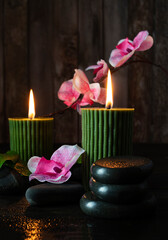 Black basalt stones with droplets of water on a dark table. A sprig of pink orchid in the background. Dark wooden background