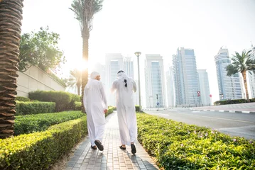 Zelfklevend Fotobehang Two young businessmen going out in Dubai. Friends wearing the kandura traditional male outfit walking in Marina © oneinchpunch