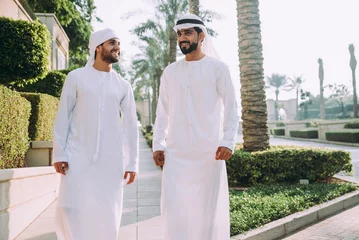 Fotobehang Two young businessmen going out in Dubai. Friends wearing the kandura traditional male outfit walking in Marina © oneinchpunch