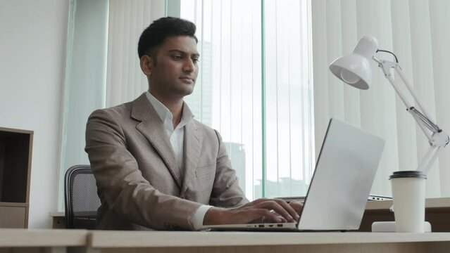 Indian businessman in formal suit typing on laptop during workday in office