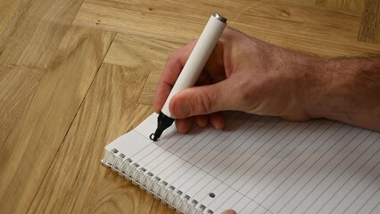 A person is thinking ahead to the coming year by sitting down and writing by hand his goals for2023 written with a black marker on a lined writing pad.