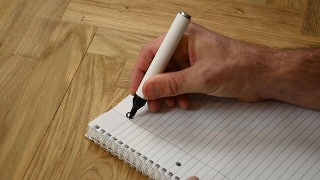A person is thinking ahead to the coming year by sitting down and writing by hand his goals for2023 written with a black marker on a lined writing pad.