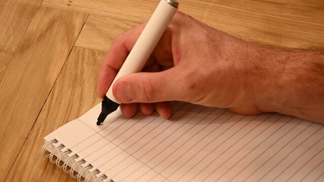 A mans hand writing out a plan for 2023 with a black marker on a lined writing pad. 
