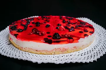 Sierkussen Close-up of a cheesecake with berries and red jelly on a black background © Diego Ignacio Riquelme Alvarado/Wirestock Creators