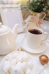  Winter, Christmas, New Year decoration composition, concept, background. White Mug, cup of hot tea, coffee, meringue, knitted plaid. Christmas lights. Christmas mood morning. Xmas greeting card.