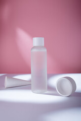 Transparent cosmetics toner bottle with concrete decorative elements on pink backdrop in harsh light mockup, no brand template