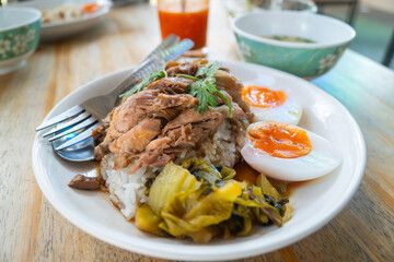 Pork leg rice with boiled egg in gravy and kale in white dish on wooden table