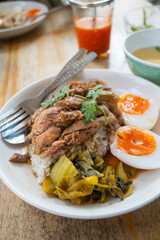 Pork leg rice with boiled egg in gravy and kale in white dish on wooden table