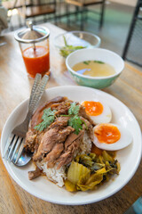 Pork leg rice with boiled egg in gravy and kale in white dish on wooden table