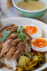 Pork leg rice with boiled egg in gravy and kale in white dish on wooden table