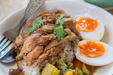 Pork leg rice with boiled egg in gravy and kale in white dish on wooden table