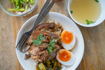 Pork leg rice with boiled egg in gravy and kale in white dish on wooden table
