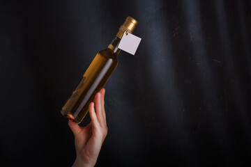 female hand holding 250 ml bottle of white wine with mock up label, no brand on black background. Alcohol drink, copy space