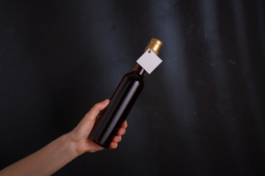 Hand Holding Bottle Of Red Wine With Template Label, No Brand. Alcohol Beverage On Black Background. Alcohol Addiction Concept