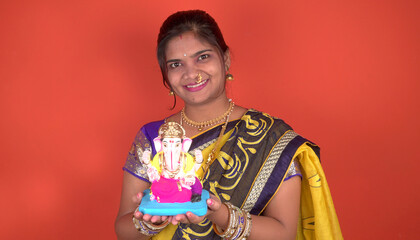 Happy young Indian woman posing with Ganesha statue on the occasion of Ganesh Festival.
