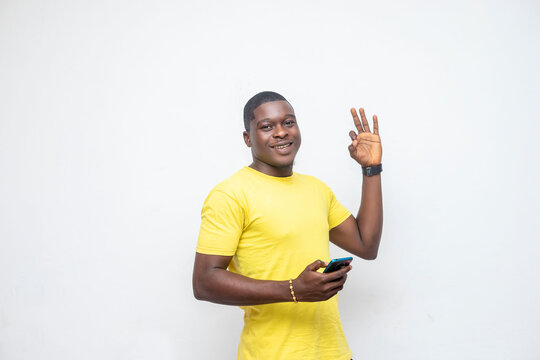 Young AFrican millennial man holding a mobile happy and counting three with fingers stands over a white background