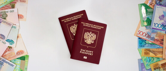 Two biometric red Russian passports between two stacks of paper bills on light background. Money of Republic of Kazakhstan and cash banknotes of Russia. Concept of currency exchange, relocation. Tenge