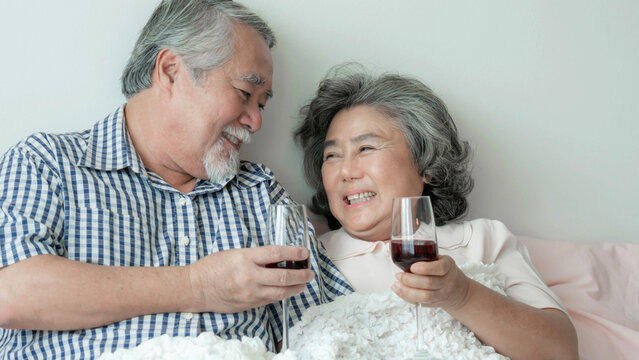 Happy love Elderly couple smile holding a wine glass , Senior couple old man and senior woman relaxing On the bed in the bedroom Celebrate the wedding anniversary - lifestyle senior concept