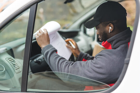 Shopping online. Delivery process. Side view of delivery truck driver - African-American middle-aged man dressed in courier outfit - looking at documents on his clipboard. High quality photo