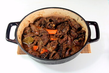 Stewed meat with vegetables and spices in a cast-iron frying pan on a white background