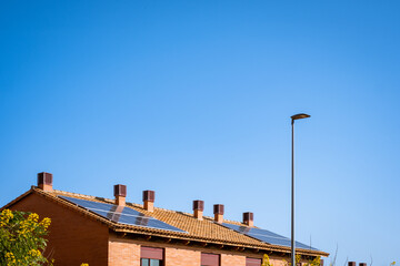 Single-family house, two-story, red adobe brick, with several black solar panel panels on its red tile roof. Clear blue sky, no clouds. Autumn.  Tenerife, Canary Islands, Spain.