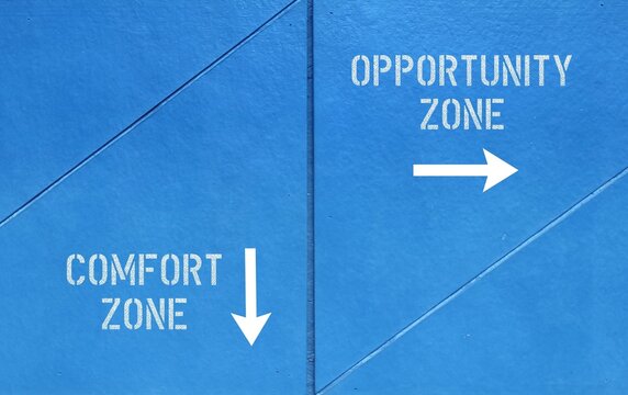 Blue wall with direction sign and text written COMFORT ZONE and OPPORTUNITY ZONE, means to step out of comfortable feel safe situation to explore and try new things