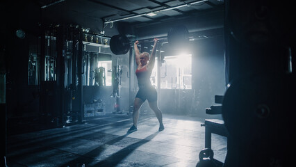 Fototapeta na wymiar Motivated Female Bodybuilder Exercising and Lifting a Heavy Barbell. A Resolute Woman Training Alone in a Hardcore Gym Working on Her Endurance During her Daily Workout