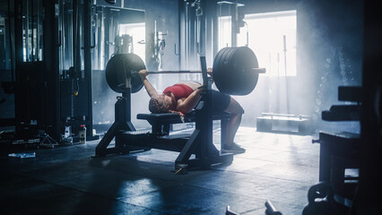 Professional Female Athlete Doing Bench Press Workout Using Barbell In a Grunge Hardcore Gym. An...
