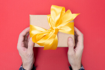 Man gives a gift wrapped in craft paper and tied with a yellow ribbon. Red background. Top view. Concept of fun holiday and birthday.
