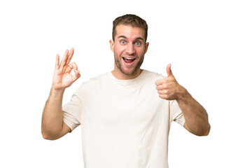 Young handsome caucasian man isolated on green chroma background showing ok sign and thumb up gesture