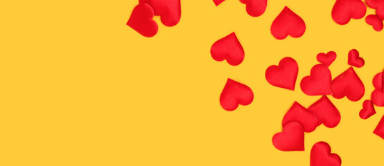 Banner with red textile hearts confetti scattered on a yellow background. Concept with copy space.