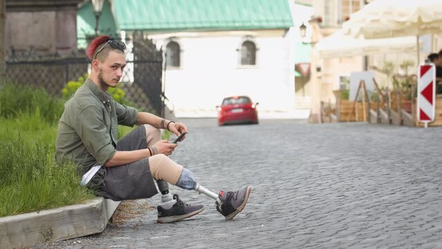 Young disabled man on street, using mobile phone, looking in camera.