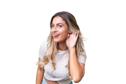 Young Uruguayan woman over isolated background listening to something by putting hand on the ear