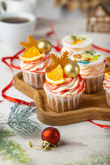 Christmas cupcakes with vanilla frosting, orange and gingerbread snowflake on white background. Vertical selective focus