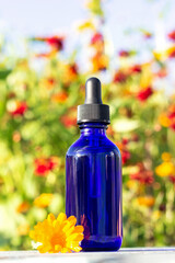 Blue glass dropper bottle with serum, essential oil or other cosmetic product on bright floral background. Natural Organic Spa Cosmetic Beauty Concept Mockup Front view