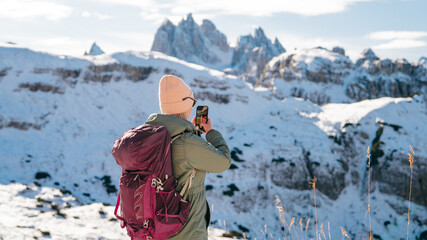 Fototapeta na wymiar Woman traveler making photo with her smartphone in Tre Cime di Lavaredo in snow South Tyrol, Italy. Winter landscape of Dolomites, Italy