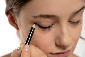 woman applying eyeliner on eyelid with pencil on a white background - obrazy, fototapety, plakaty