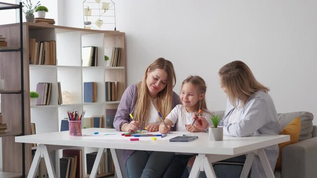 Family painting. Enjoying time. Creative art. Happy little girl drawing with mother and grandmother together sitting desk in light room interior.