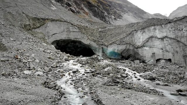 Aerial flyover into the ice cave of the Zinal glacier in Valais, Switzerland with a pan up view from the melting glacial water stream and crevasses