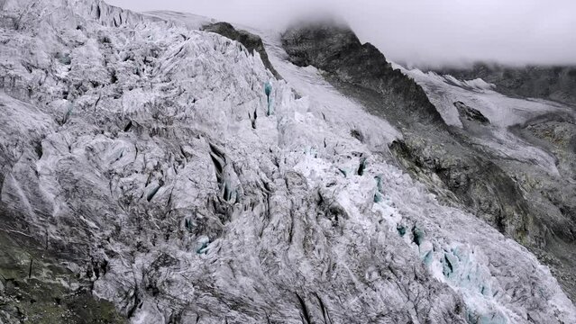 Aerial flyover over a hiker at a viewpoint of the Moiry glacier near Grimentz in Valais, Switzerland with a view of the icy crevasses as mountains hide in the clouds