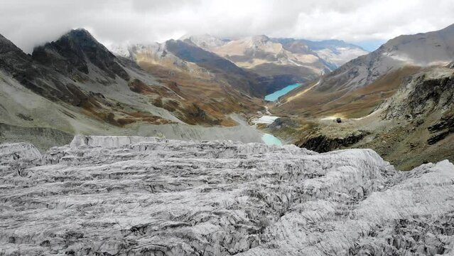 Aerial flyover alongside the edge of the Moiry glacier near Grimentz in Valais, Switzerland with of the icy crevasses, valley and lake on a cloudy summer afternoon