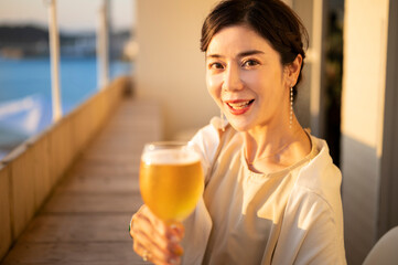 夕暮れ時、海が見えるカフェのテラスでビールを飲む女性