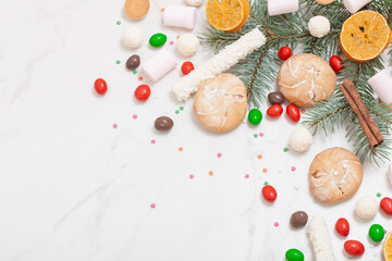 candies and cookies with christmas tree branches on white marble background