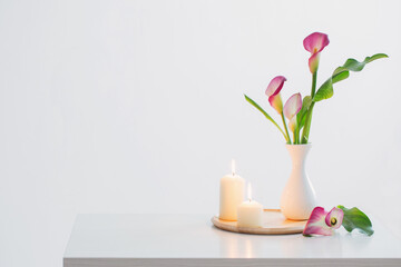 pink calla lily in vase  and burning candles on white background