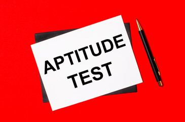 Black pen, envelope and white card with the text APTITUDE TEST on a bright red background