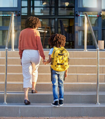 Mother, child and holding hands at school building, education with backpack and ready to learn at academy. Learning, study and student, black woman support kid for first day back to school. © L Ismail/peopleimages.com
