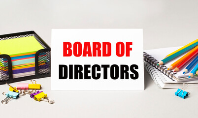 A paper card with the text BOARD OF DIRECTORS, multi-colored pencils, stickers and paper clips on the desktop.