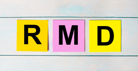 Three multi-colored paper stickers with RMD Required Minimum Distributions text on a blue wooden...