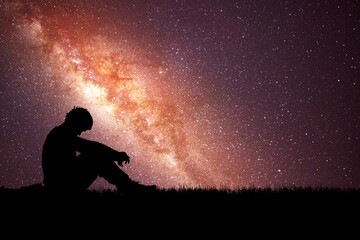Loneliness, despair and regret concept. Lonely man in the meadow against the backdrop of stars and the Milky Way.