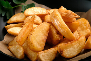 Fried potatoes in large pieces with ketchup in a black plate, close up